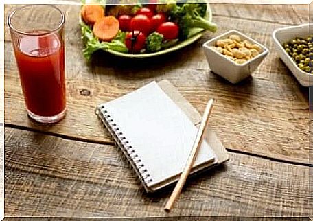 A glass of tomato juice with a healthy salad and a notebook on the table