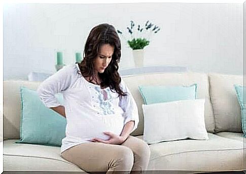 A pregnant woman is sitting on the couch with her hand against her stomach